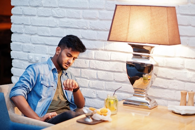 Portret van een knappe, succesvolle, bebaarde Zuid-Aziatische jonge Indiase freelancer in een spijkerbroek die in een café zit met kipnuggets en limonade