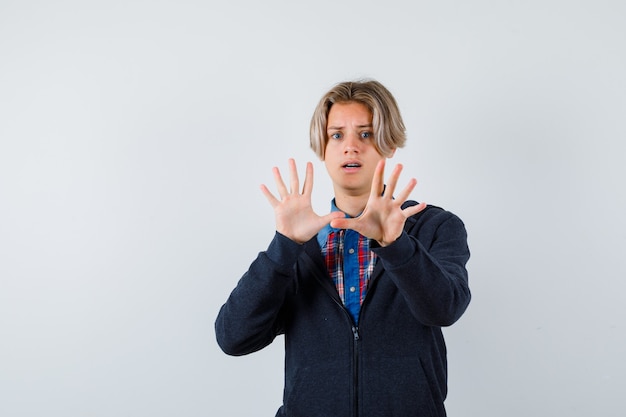 Portret van een knappe tienerjongen die een overgavegebaar toont in een shirt, hoodie en een bang vooraanzicht