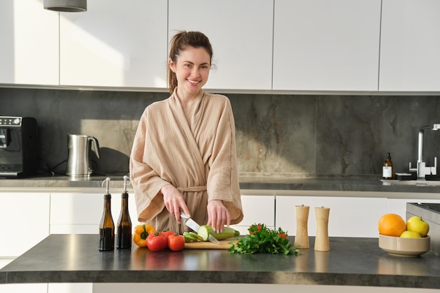 Portret van een knappe vrouw die salade kookt in de keuken, groenten hakt en glimlacht terwijl ze voorbereidingen treft