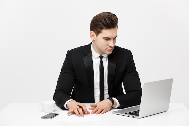 Portret van een knappe zakenman die een smartphone vasthoudt terwijl hij op een computer aan zijn bureau werkt.