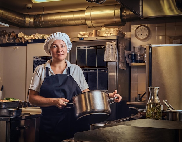 Portret van een kok van middelbare leeftijd die een uniform draagt en een pan vasthoudt in de keuken van het restaurant.