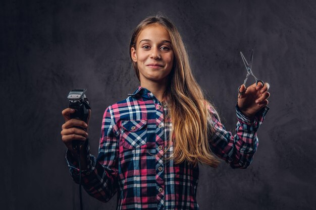 Portret van een lachend jong meisje gekleed in shirt houdt trimmer en schaar. Geïsoleerd op een donkere gestructureerde achtergrond.