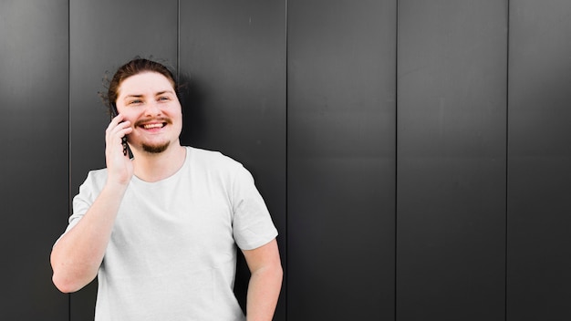 Portret van een lachende jonge man praten op mobiele telefoon tegen de zwarte muur