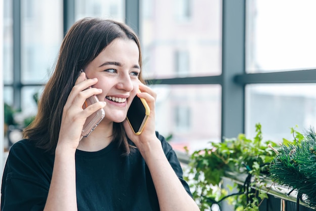 Portret van een lachende jonge vrouw die op twee telefoons praat