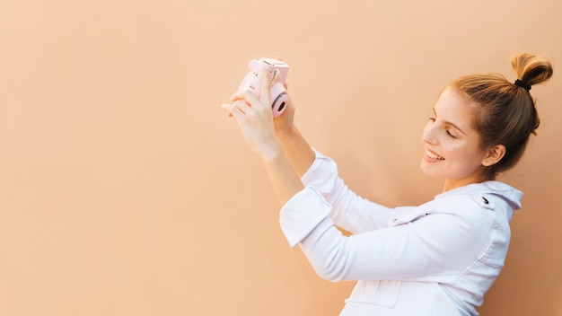 Portret van een lachende jonge vrouw praten zelfportret met roze instant camera tegen bruine achtergrond