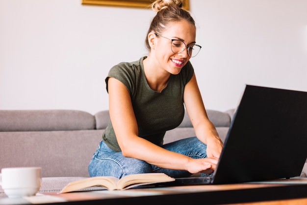Portret van een lachende jonge vrouw zittend op de Bank met behulp van laptop