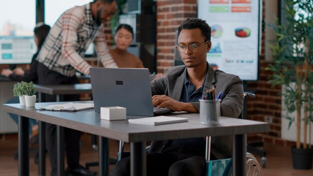 Portret van een lachende man met een handicap die aan een project werkt, met behulp van een laptop met grafieken en statistieken om gegevensanalyse te maken. Mannelijke werknemer planning financiële strategie voor ontwikkeling.