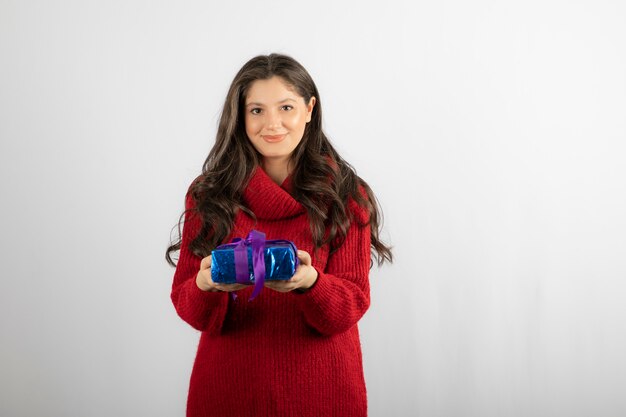 Portret van een lachende vrouw die een kerstcadeaudoos met paars lint geeft.