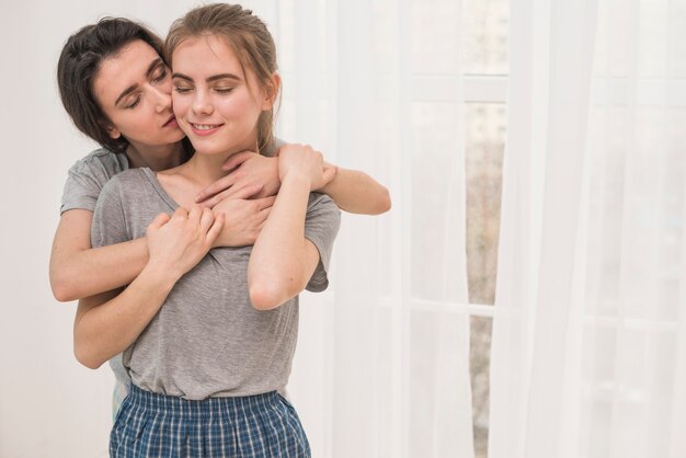 Portret van een lesbienne die van haar meisje houdt dat zich voor wit gordijn bevindt