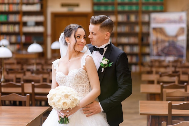 Portret van een liefdevol bruidspaar dat elkaar in de bibliotheek aankijkt