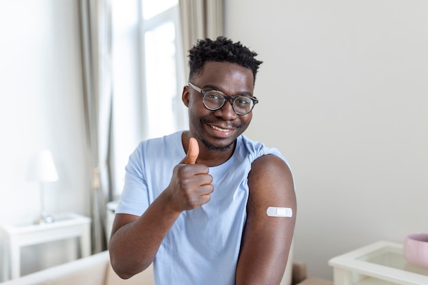 Portret van een man die lacht na het krijgen van een vaccin afrikaanse man die zijn mouw vasthoudt en zijn arm met verband laat zien na vaccinatie