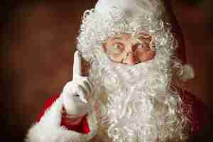 Gratis foto portret van een man in kerstman kostuum met een luxe witte baard, kerstmuts en een rood kostuum in het rood