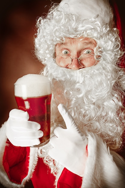 Portret van een man in kerstman kostuum met een luxe witte baard, kerstmuts en een rood kostuum in rood met bier