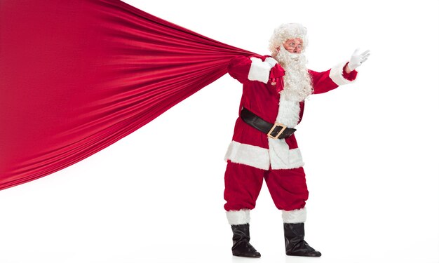 Portret van een man in kerstman kostuum - met een luxe witte baard, kerstmuts en een rood kostuum - in volle lengte geïsoleerd op een witte achtergrond met een grote zak met geschenken