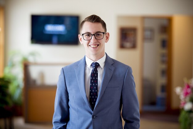 Portret van een man met een bril in een blauw pak met een stropdas onder de lichten met een onscherpe achtergrond