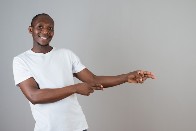 Portret van een man met een donkere huid in een wit t-shirt die iets op een grijze muur wijst