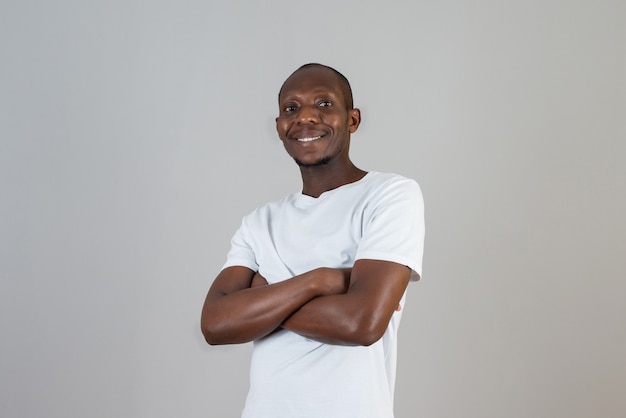 Portret van een man met een donkere huid in een wit t-shirt met staande armen gekruist op een grijze muur