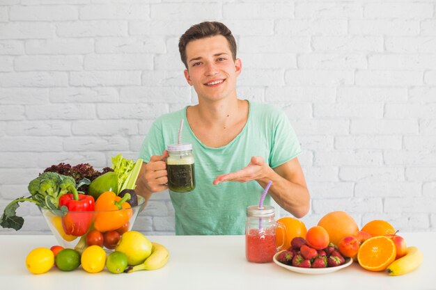 Portret van een man met groene smoothie pot met veel gezonde voeding op tafel