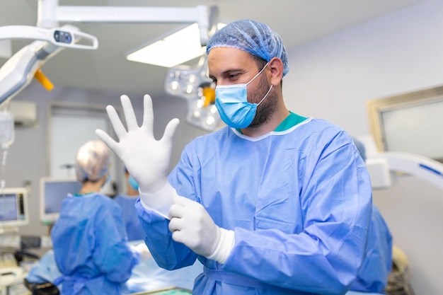 Portret van een mannelijke arts-chirurg die medische handschoenen aantrekt die in de operatiekamer staan Chirurg in de moderne operatiekamer