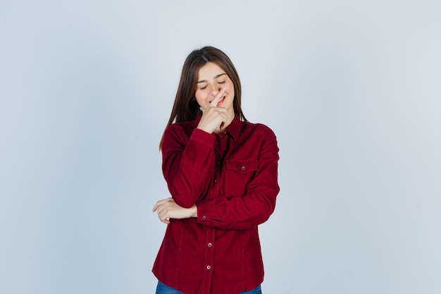 Portret van een meisje dat de hand op de kin houdt, de ogen sluit in een casual shirt en zich schaamt