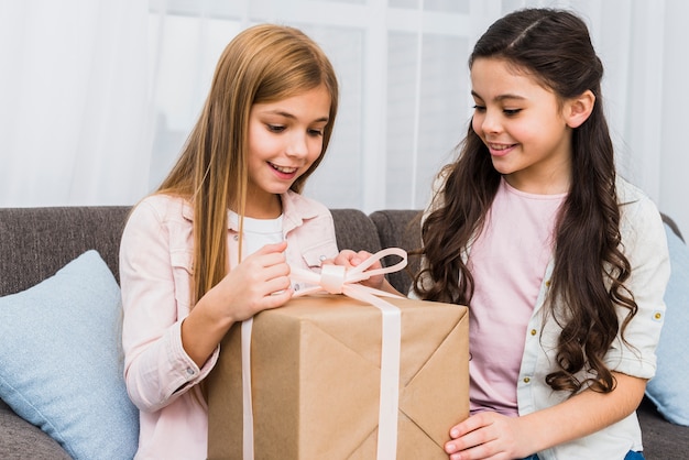 Portret van een meisje dat haar glimlachende vriend bekijkt die de giftdoos opent