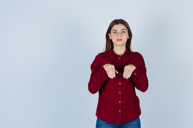 Portret van een meisje dat handen als poten in een bordeauxrode blouse houdt en er grappig uitziet
