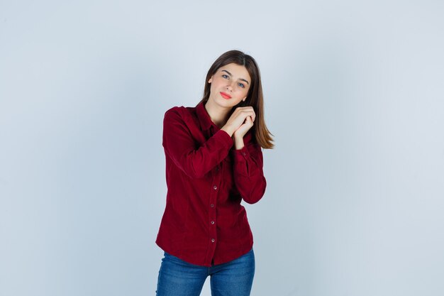 Portret van een meisje dat op gevouwen handen leunt in een bordeauxrode blouse en er zelfverzekerd uitziet