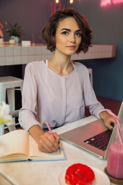 Portret van een meisje die op laptop typen en nota's schrijven