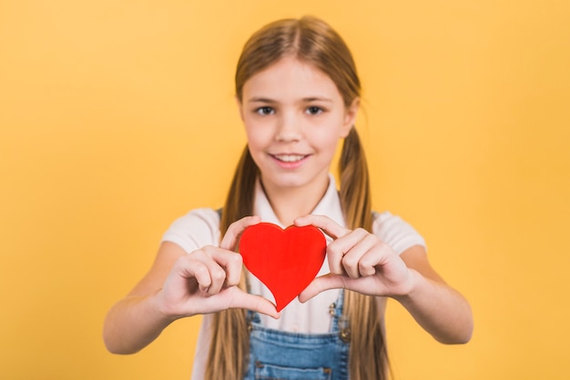 Portret van een meisje die rood hart houden naar camera tegen gele achtergrond