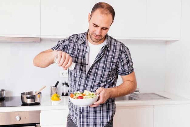 Portret van een mens die kruiden in saladekom toevoegt