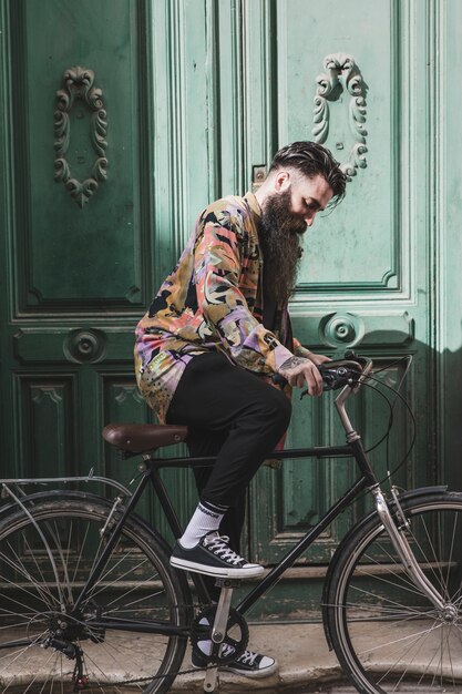 Portret van een modieuze jonge man die de fiets berijdt