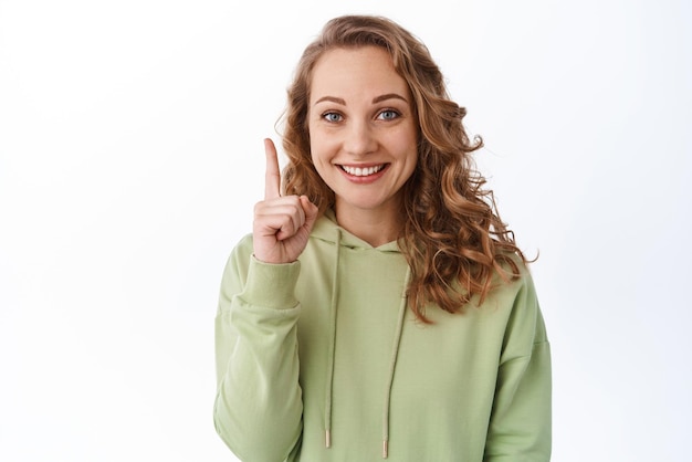 Portret van een mooi blond meisje glimlachend wijzend met de vinger naar boven met promotekst, een link weergeven om op een witte achtergrond te klikken