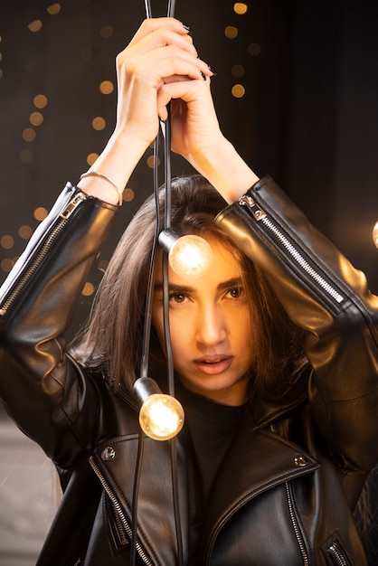 Portret van een mooi jong model in zwart lederen jas poseren in de buurt van lampen.