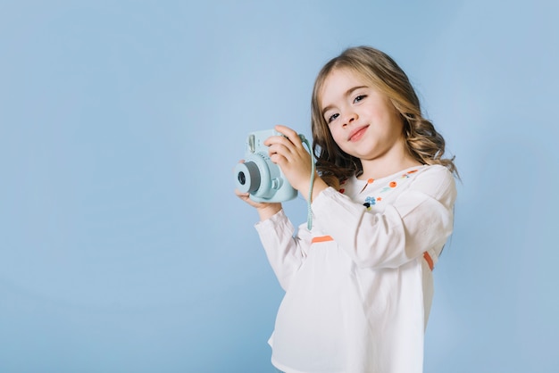 Portret van een mooi meisje die retro onmiddellijke camera in handen houden tegen blauwe achtergrond