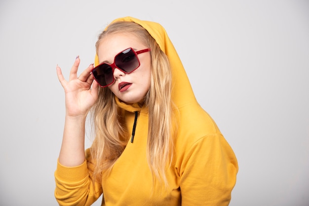 Portret van een mooi meisje in een gele hoodie met een stijlvolle bril.