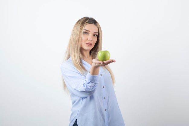 Portret van een mooi meisjesmodel dat staat en een groene verse appel vasthoudt.