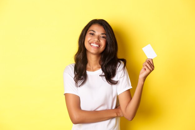 Portret van een mooie afro-amerikaanse vrouw in een wit t-shirt die tevreden glimlacht en een creditcard toont