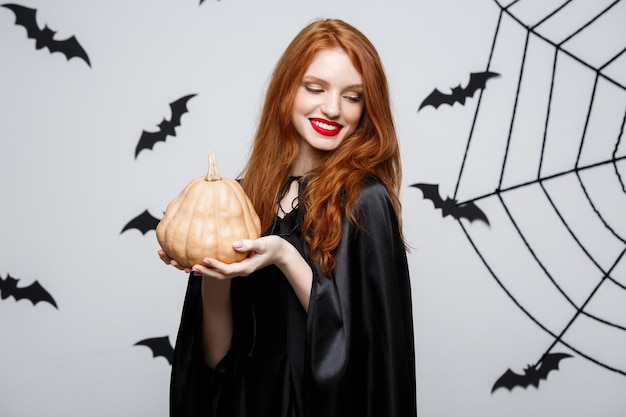 Portret van een mooie blanke heks die pompoen vasthoudt voor het vieren van halloween