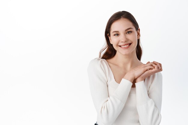 Portret van een mooie blanke vrouw klapt in de handen en glimlacht tevreden, kijkt dankbaar naar de camera, ontvangt een geschenk en verheugt zich, staande tegen een witte achtergrond