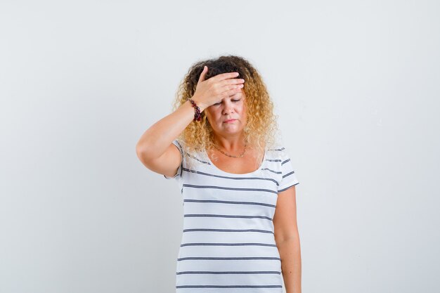 Portret van een mooie blonde vrouw die lijdt aan hoofdpijn in een gestreept t-shirt en er droevig uitziet
