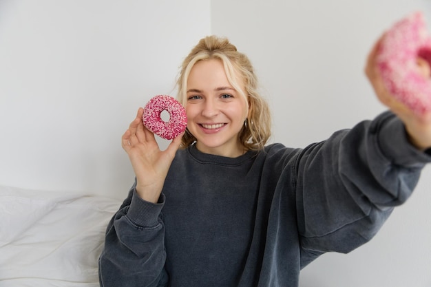 Portret van een mooie blonde vrouw met twee roze donuts, heerlijk gebak, dessert en