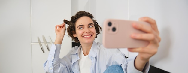 Portret van een mooie brunette vrouw die een selfie maakt en met haar krullen speelt om foto's te maken op haar mobiele telefoon