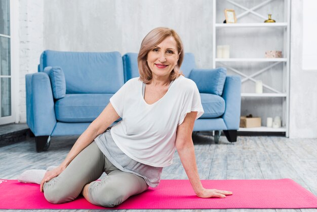 Portret van een mooie gelukkige vrouw zittend op roze yoga mat camera kijken