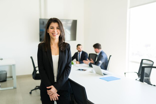 Portret van een mooie, gelukkige zakenvrouw in een pak die lacht en zich klaarmaakt om een werkpresentatie te geven aan haar collega's in de vergaderruimte