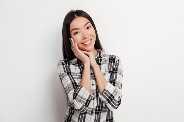 Portret van een mooie glimlachende dame met donker haar die staat en gelukkig in de camera kijkt op een witte achtergrond in de studio