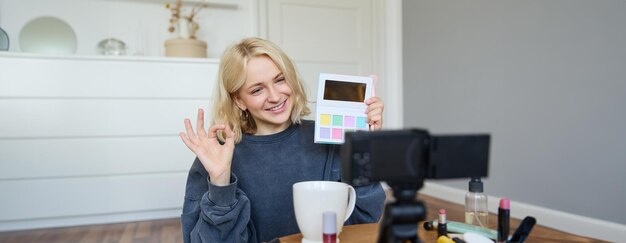 Portret van een mooie glimlachende vrouw die video opneemt in haar kamer met een camera op de koffietafel