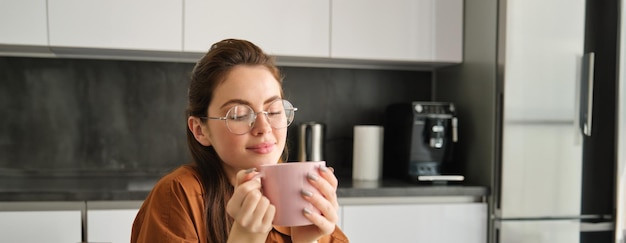 Portret van een mooie jonge vrouw die het aroma van haar koffie in een kop drankjes in de keuken ruikt