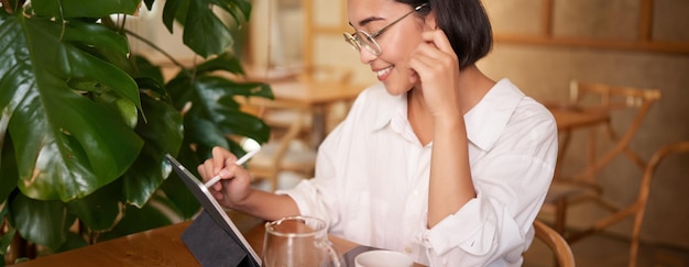 Portret van een mooie jonge vrouw die in een café koffie zit te drinken en een diagram op een tablet tekent