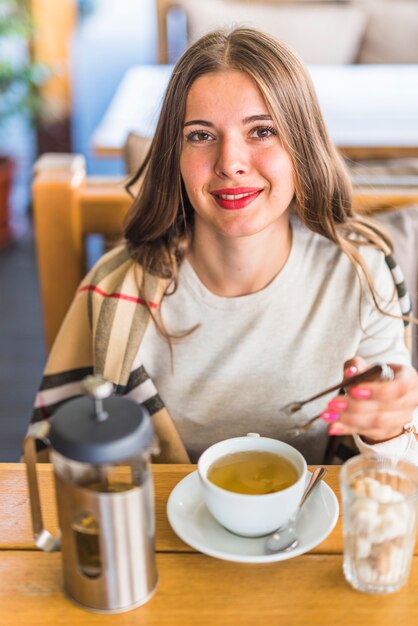 Portret van een mooie jonge vrouw met tong in de hand met kruidenthee cup op tafel