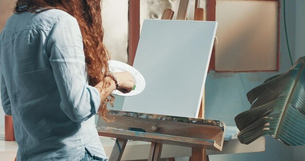 Portret van een mooie langharige vrouwelijke kunstenaar aan het werk op haar canvas in een studio